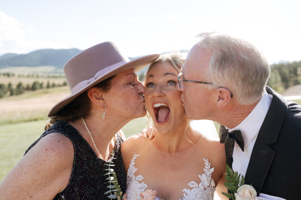 mother and father of the bride giving her a kiss on the cheek